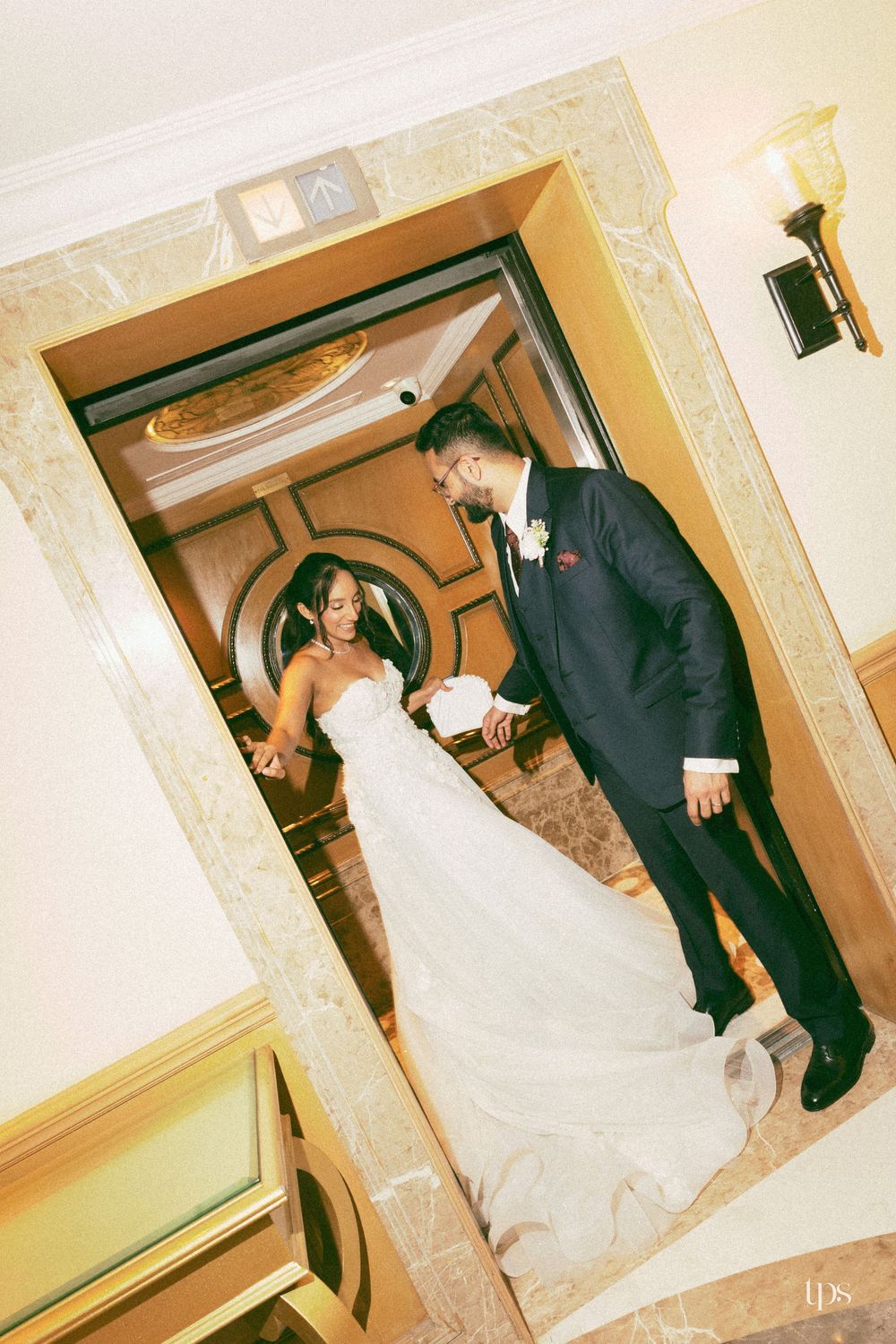 Bride and groom sharing a romantic moment in an elegant elevator doorway, bride in white gown, groom in navy suit.