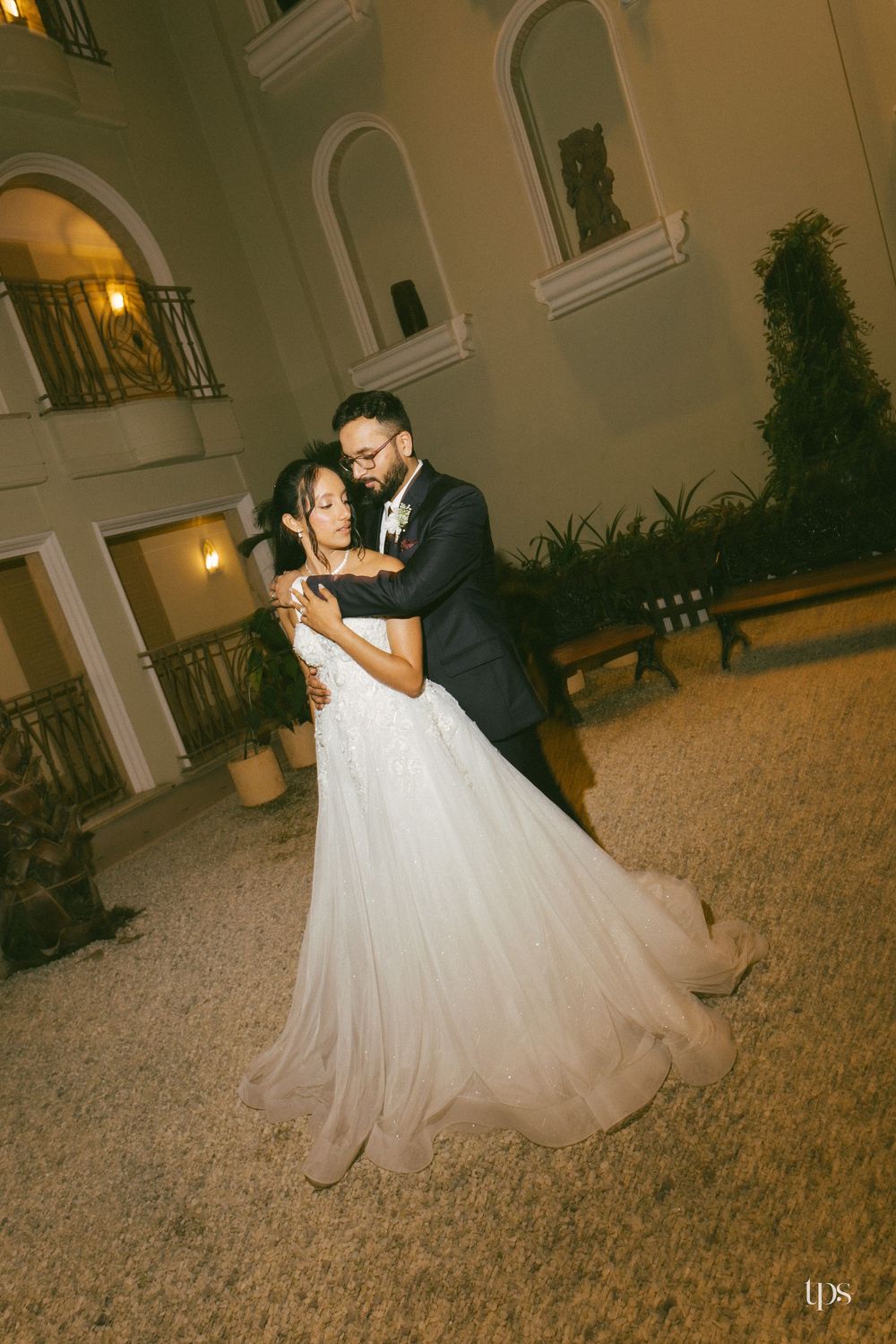 Couple sharing romantic first dance outdoors at night, bride in white ballgown, groom in navy suit.