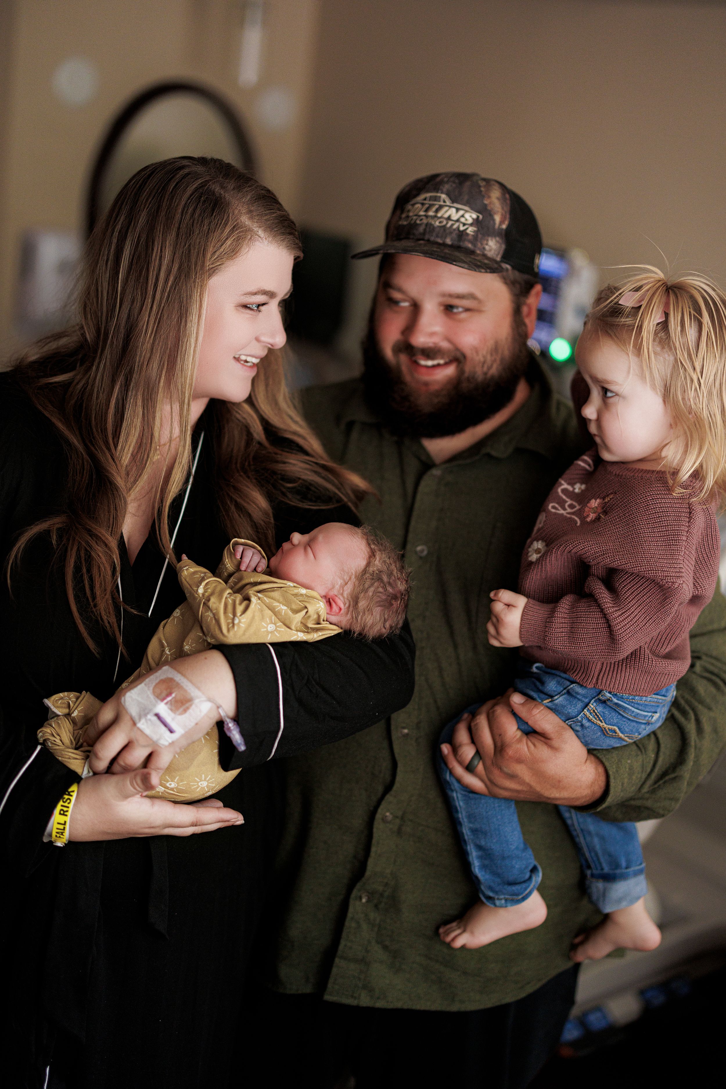 Happy family with newborn baby and toddler smiling together in a hospital room after birth.
