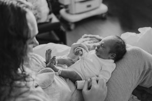 Black and white photo of a newborn baby wrapped in a white blanket being held in a hospital room.