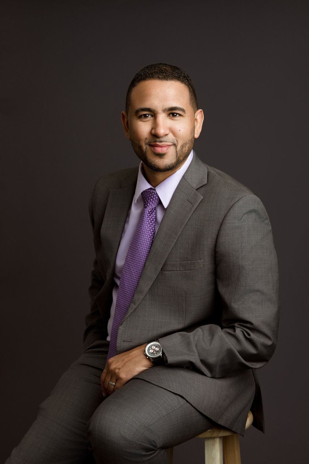 Miami professional mini headshot of a man in a gray suit and purple tie against a dark studio background.