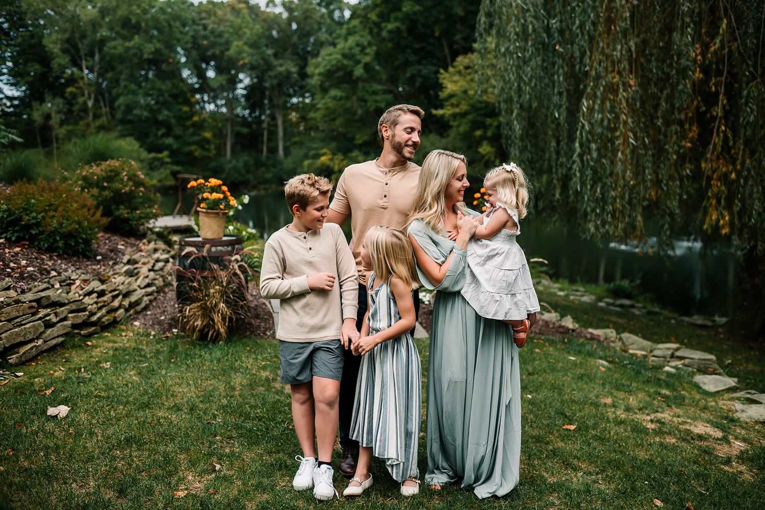 Happy family of five posing outdoors in a lush garden, parents with three children in coordinated neutral outfits.