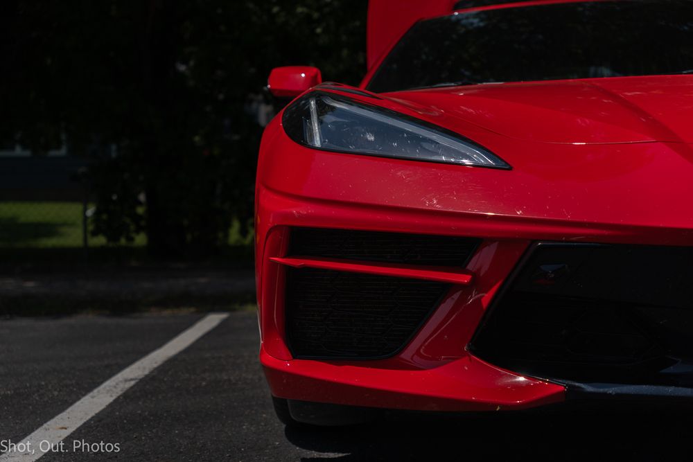 Close-up of a red Chevrolet Corvette C8 front headlight and bumper detail in a parking lot.