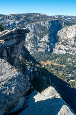 Granite cliffs overlook a forested valley with meadows and towering rock walls on a clear sunny day in Yosemite National Park.