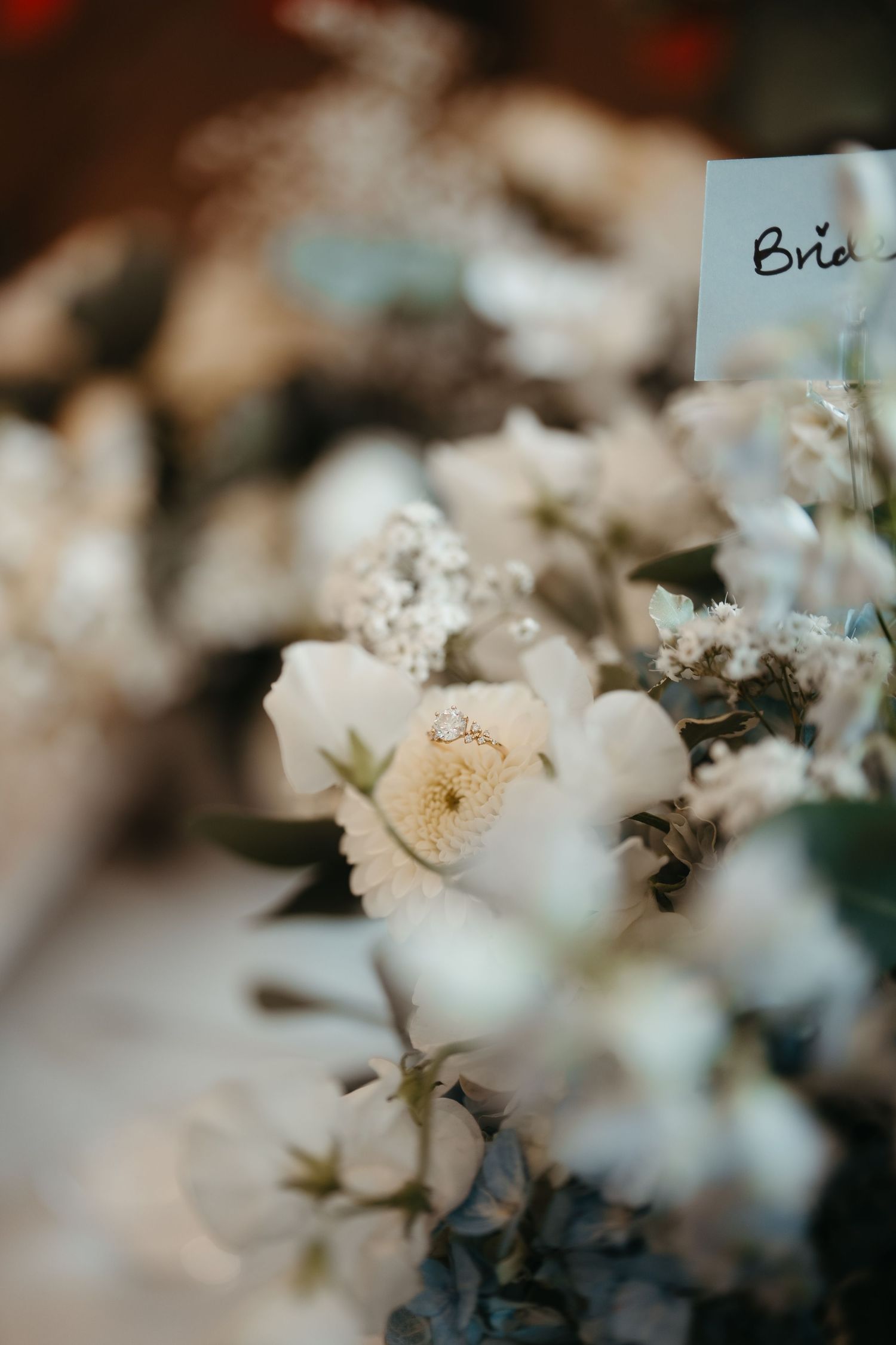 Close-up of elegant white roses and delicate blooms with a bridal place card at a wedding reception table.