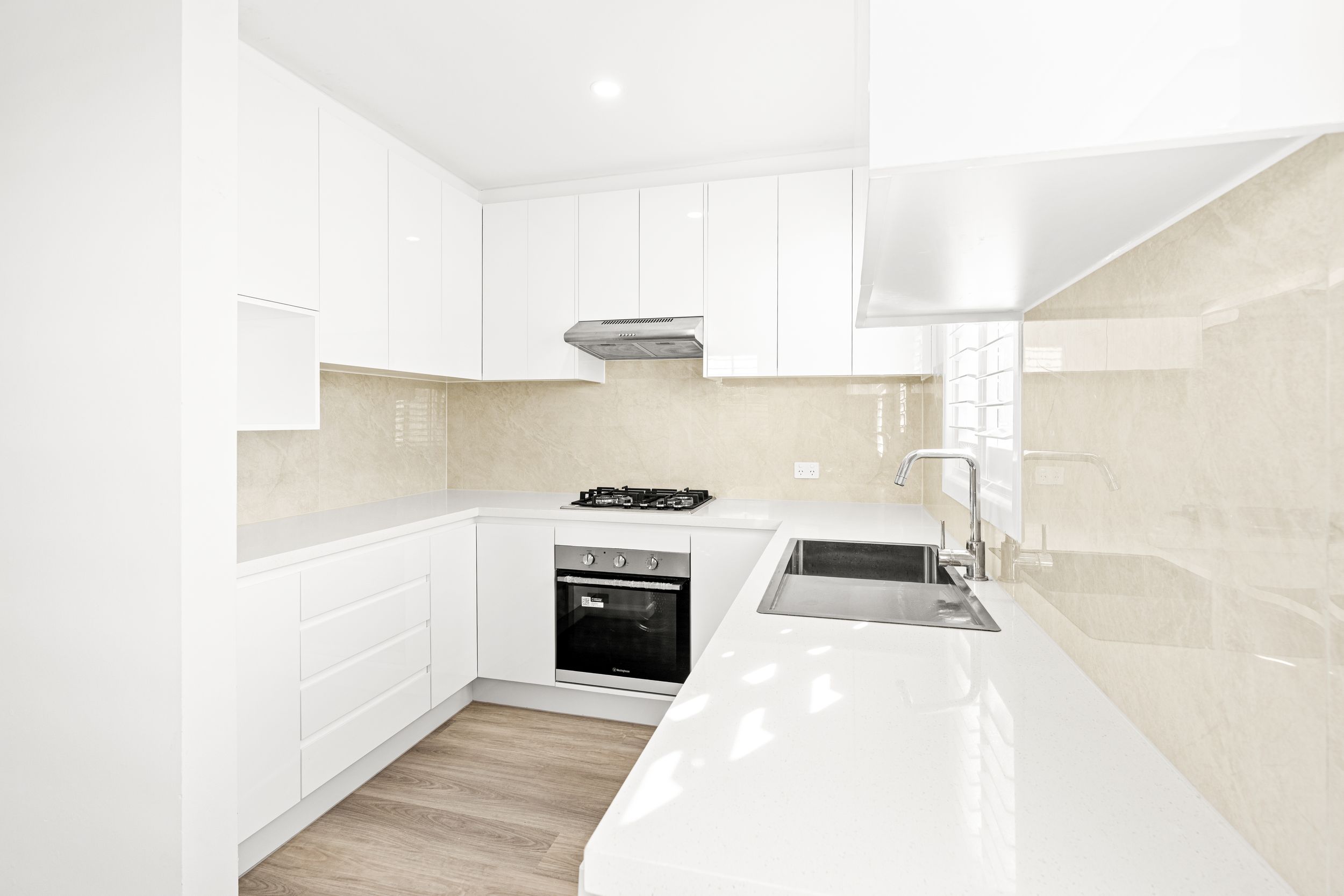 Contemporary white kitchen with stone benchtop, beige tile splashback, gas cooktop, and undermount sink.