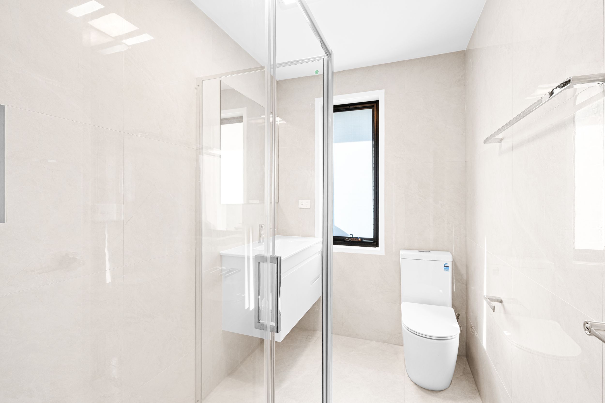 Modern white bathroom with glass shower enclosure, floating vanity, and toilet with beige tile walls.