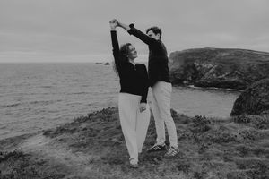 Couple dancing together on coastal cliffs overlooking the ocean in a black and white romantic outdoor photo.