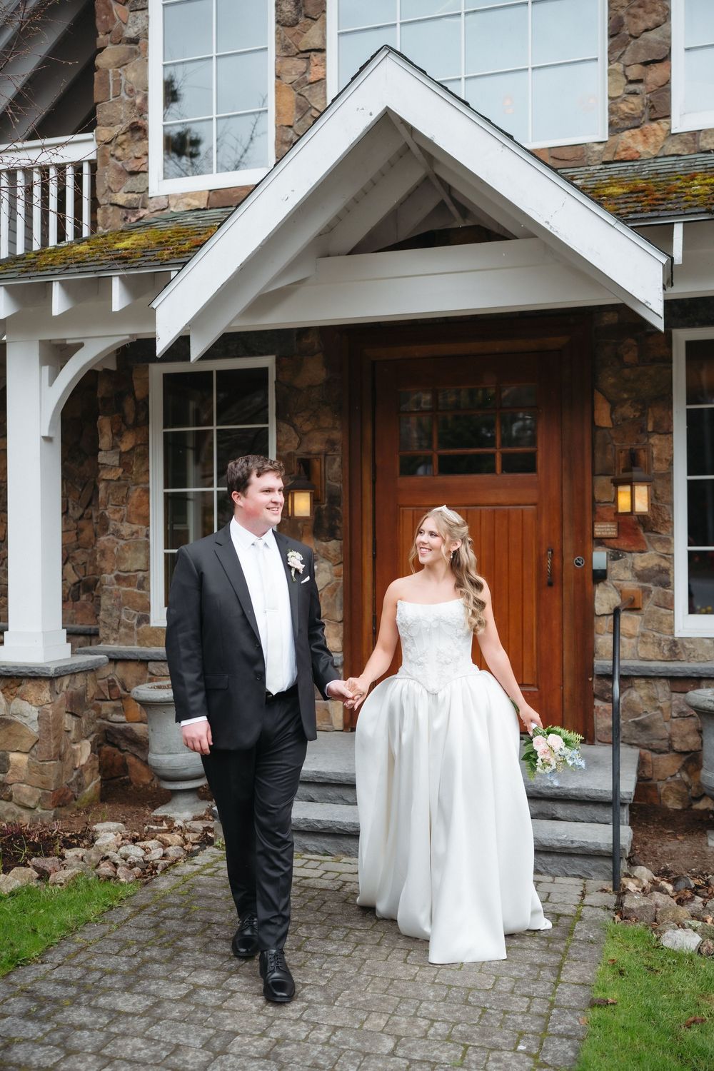 Bride and groom holding hands walking in front of a stone building with wooden door on their wedding day.
