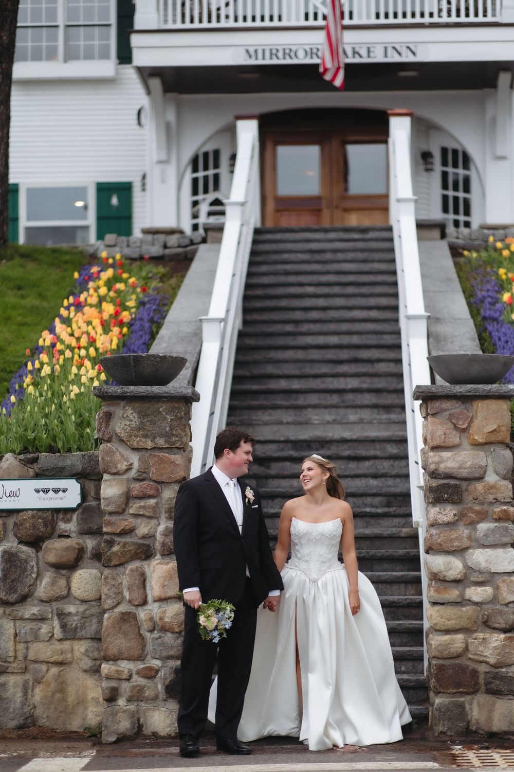 Bride and groom holding hands and smiling in front of Mirror Lake Inn with colorful tulips on their wedding day.