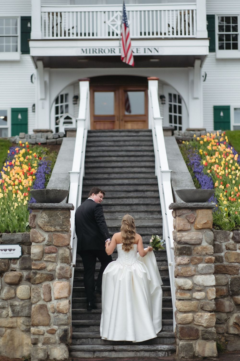 Bride and groom ascending stone steps at Mirror Lake Inn entrance, surrounded by colorful tulips.