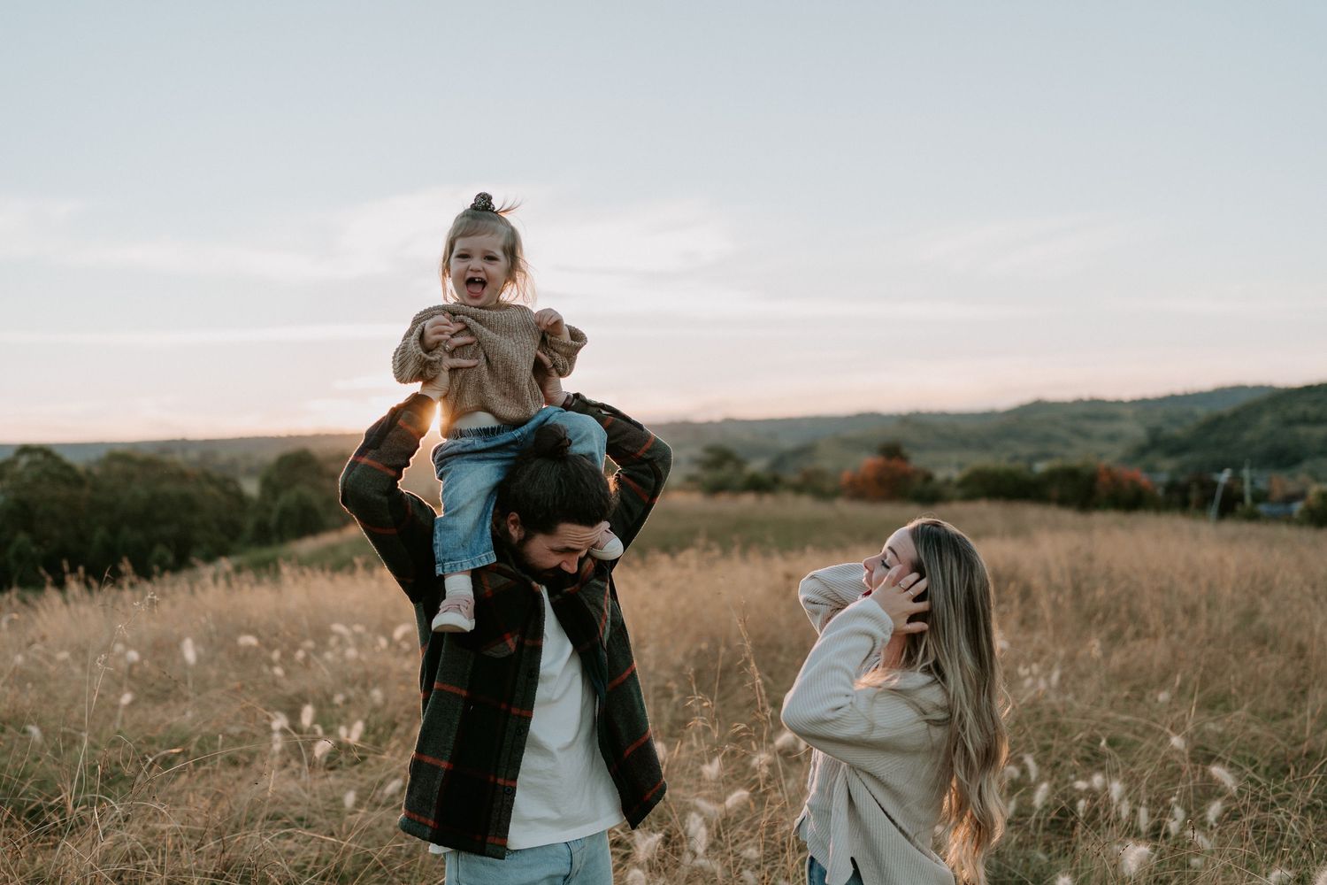 Family with young child on dads shoulders at sunset in a field in Picton, NSW