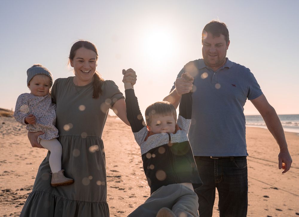 Happy family of four playing on the beach at sunset with warm golden light.