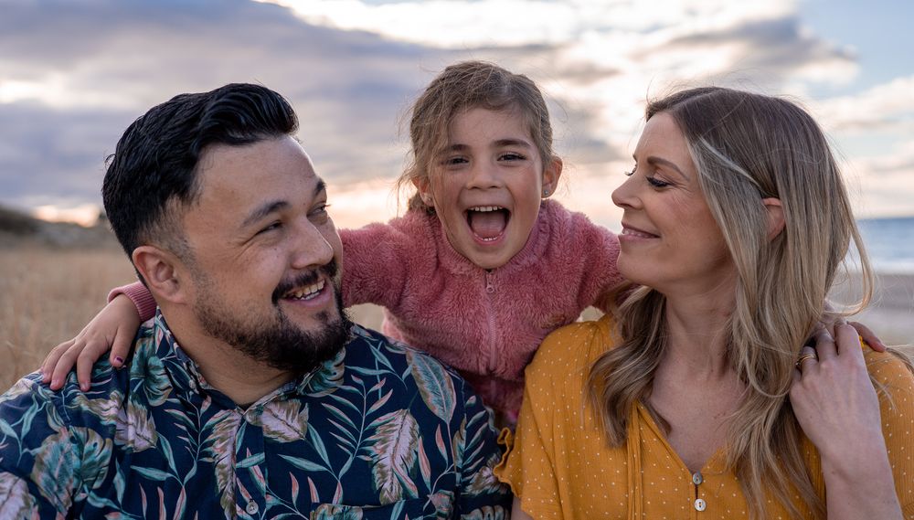 Joyful family of three laughing together in a golden field at sunset.