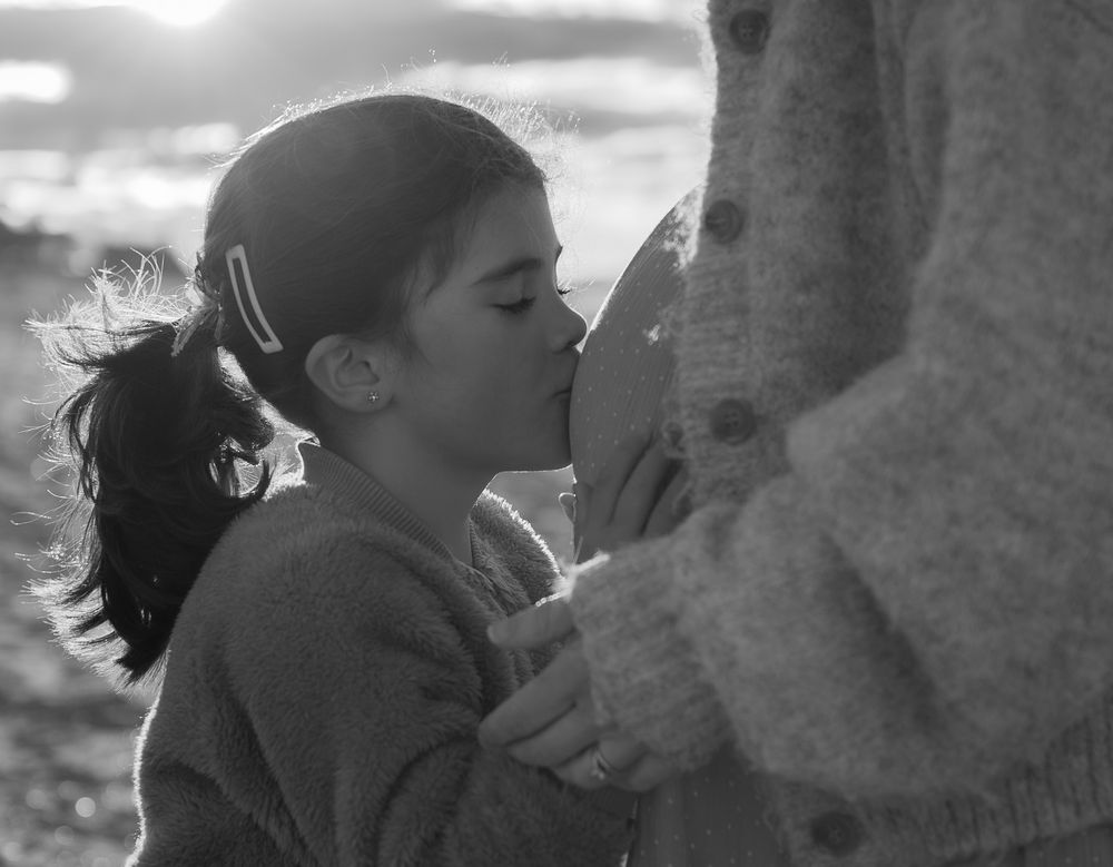 Young girl kissing a parent tenderly in a black and white beach portrait.