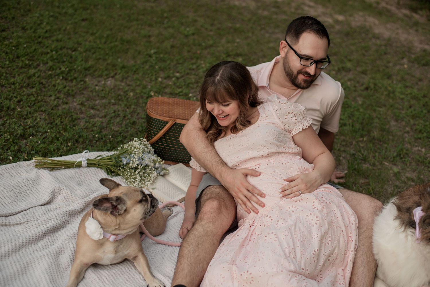 Expecting couple sitting together on a picnic blanket with their dogs during a Fort Worth maternity session.