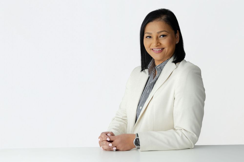 Professional woman in white blazer smiling confidently at desk, ideal for business and corporate themes.