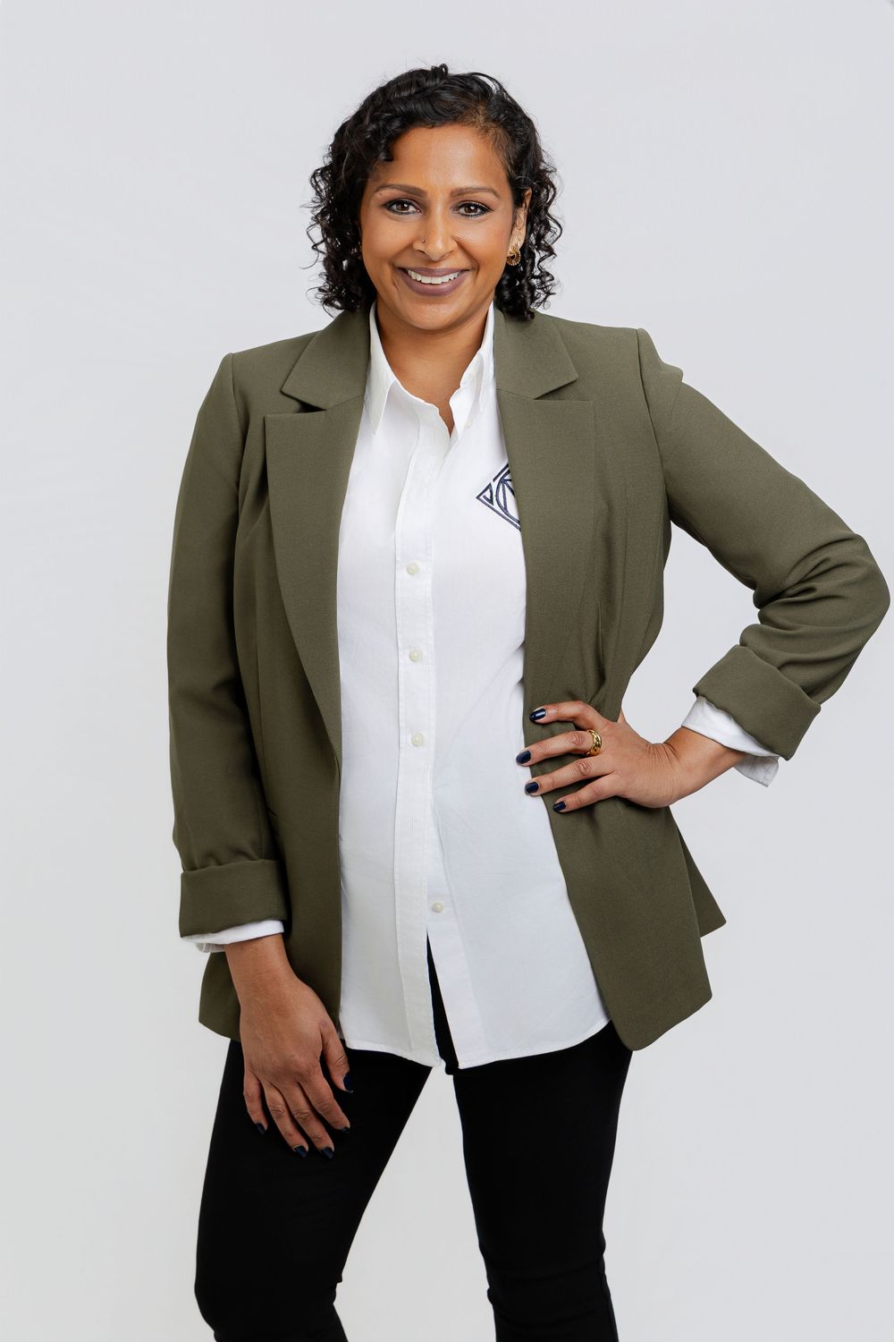 Professional woman in olive blazer and white shirt smiling confidently against a light gray background.