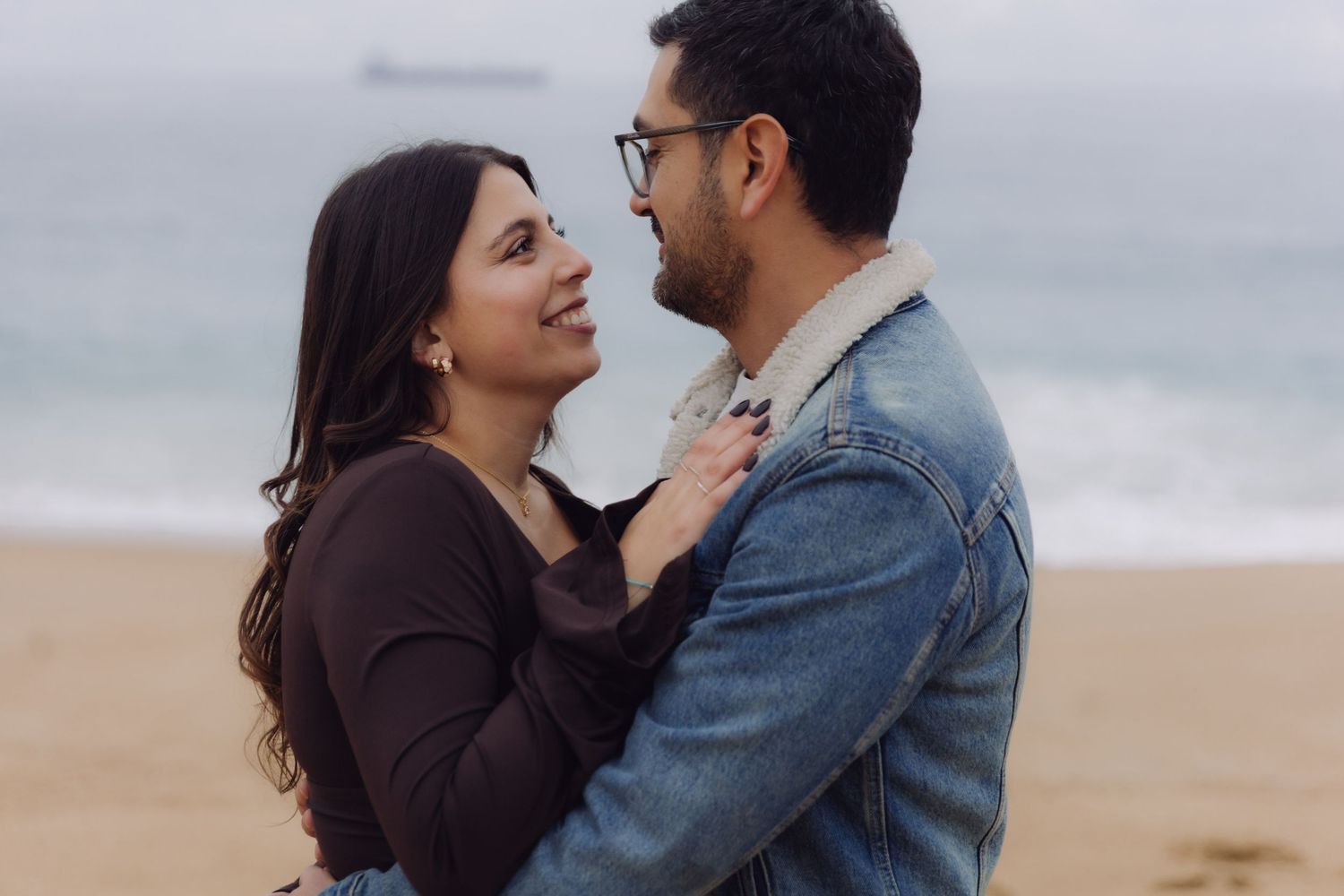 Smiling couple gazing at each other tenderly on a sandy beach by the ocean.