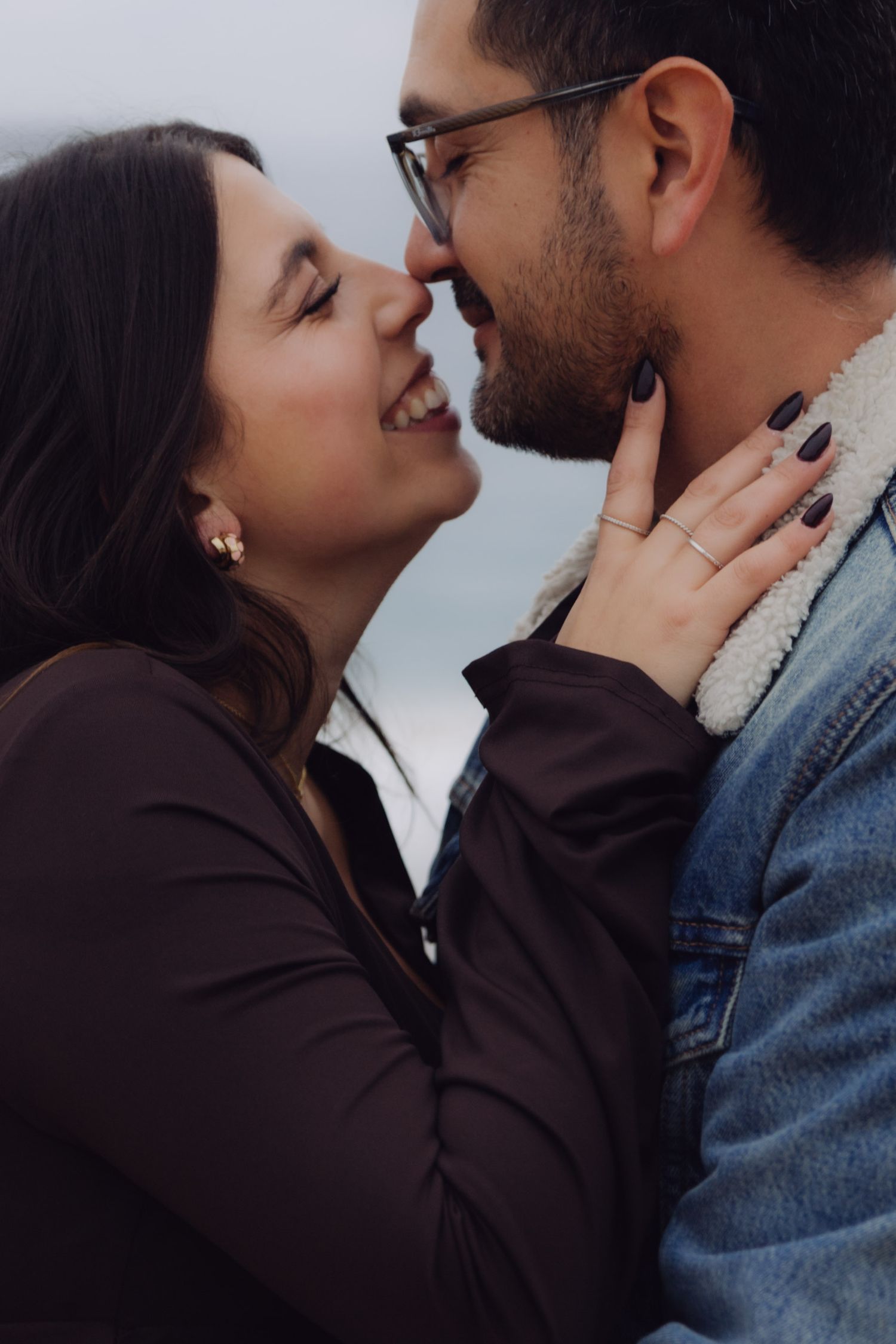 Close-up of couple nearly kissing and laughing together on a cloudy beach.