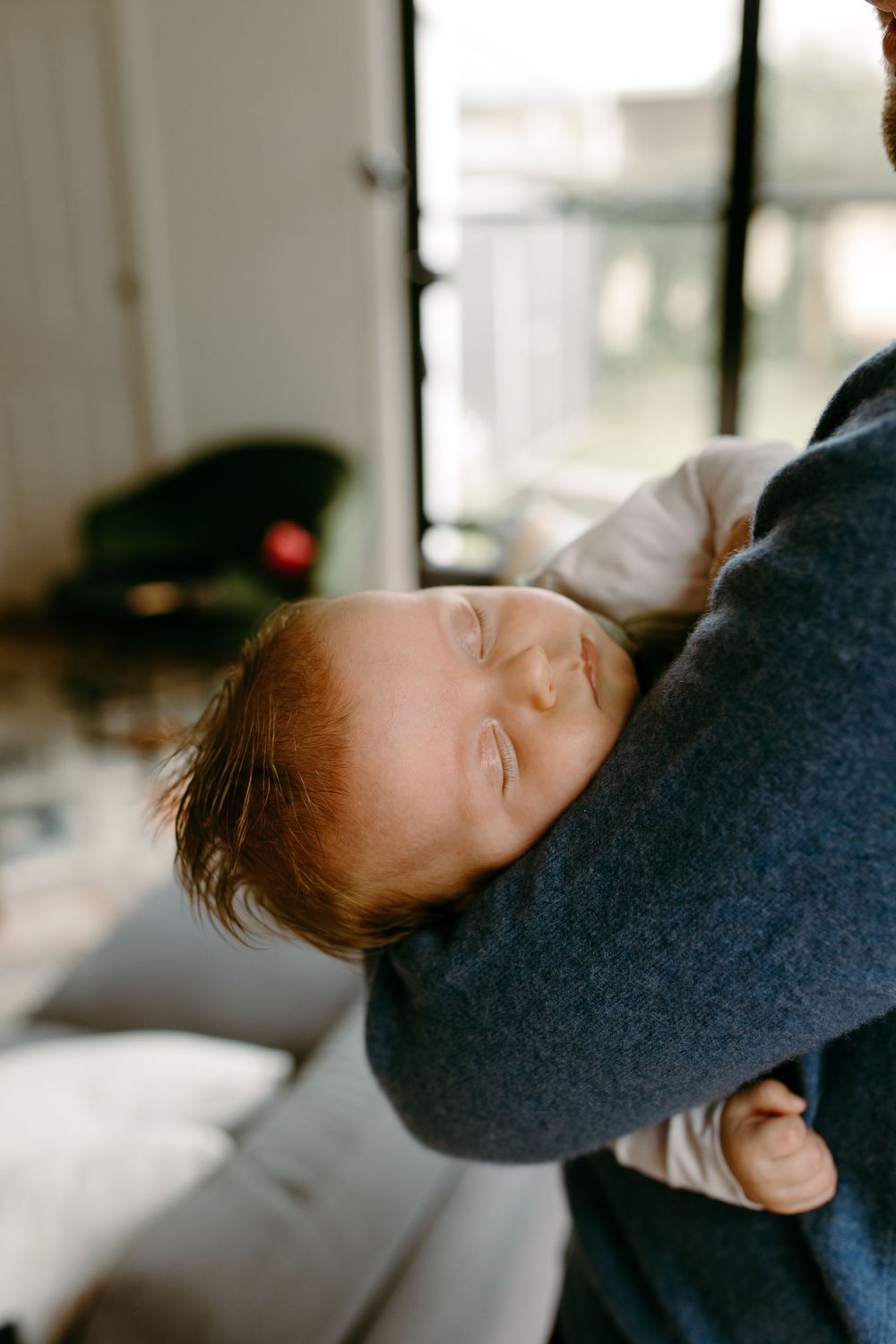 A peaceful newborn baby sleeps while being cradled in an adult's arms in a cozy home setting.