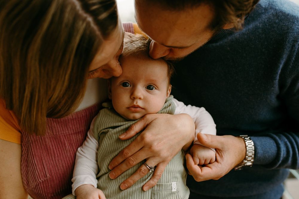 Parents lovingly holding their newborn baby, with the father kissing the infant's head in a warm family portrait.