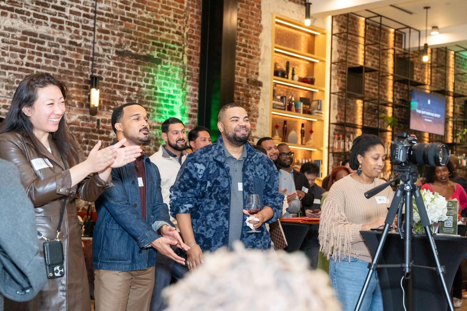 Group of diverse professionals networking at a modern bar venue with brick walls and stylish shelving.