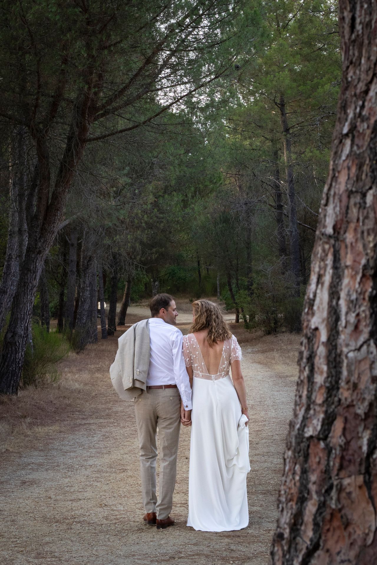 Mariés vus de dos marchant sur un chemin bordé de pins, séance photo de mariage à Lyon