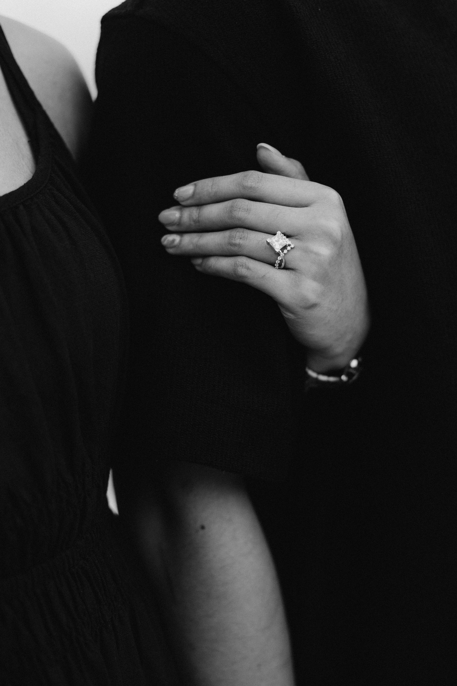Black and white photo of a woman's hand wearing a diamond engagement ring and bracelet, resting on a dark suit.