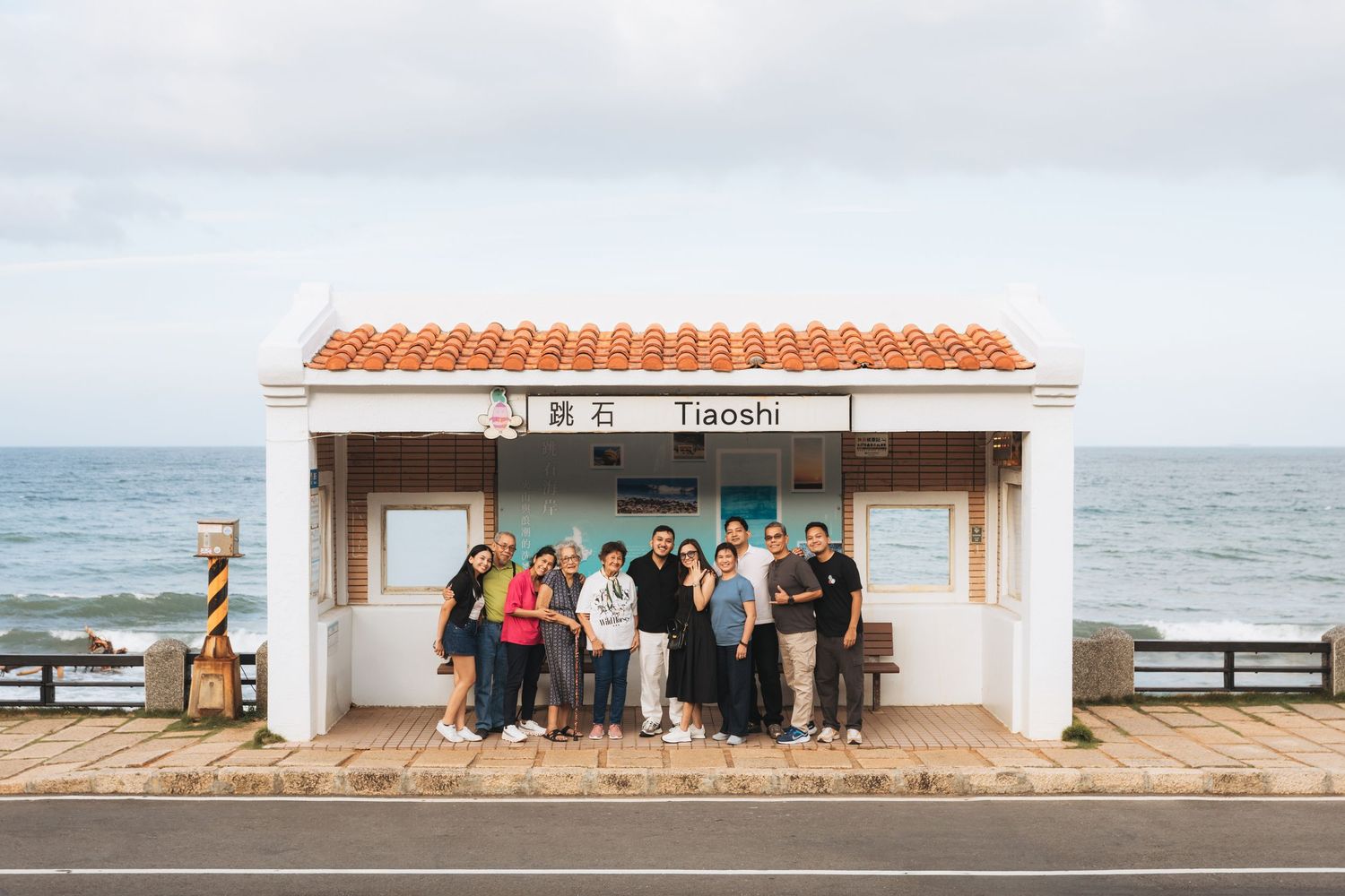 Group of tourists posing at Tiaoshi station bus stop in Taiwan with ocean views in the background.