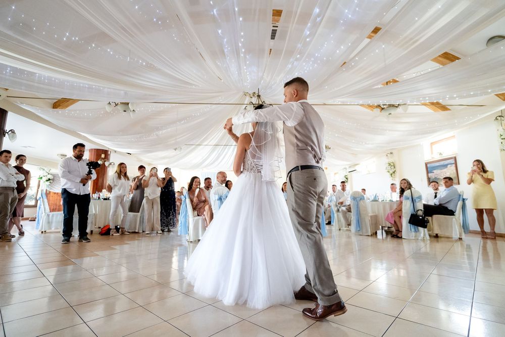Bride and groom share their first dance at elegant wedding reception with white draped ceiling decor.