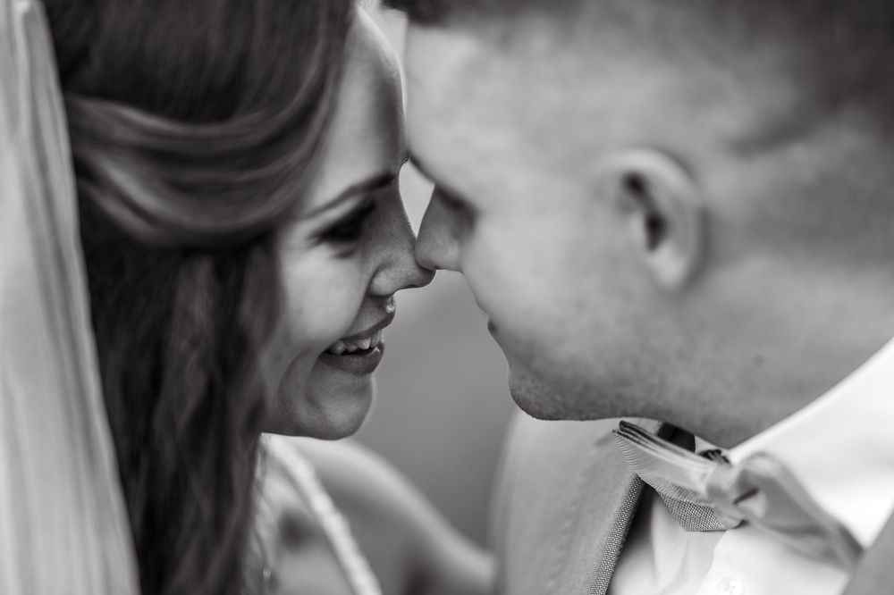 Black and white close-up of a smiling bride and groom touching foreheads on their wedding day.