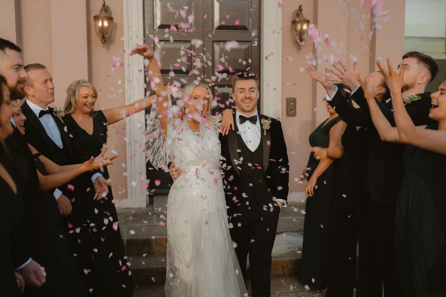 Bride and groom walk through confetti shower surrounded by wedding guests outside elegant venue doors at Boyne Hill House Estate