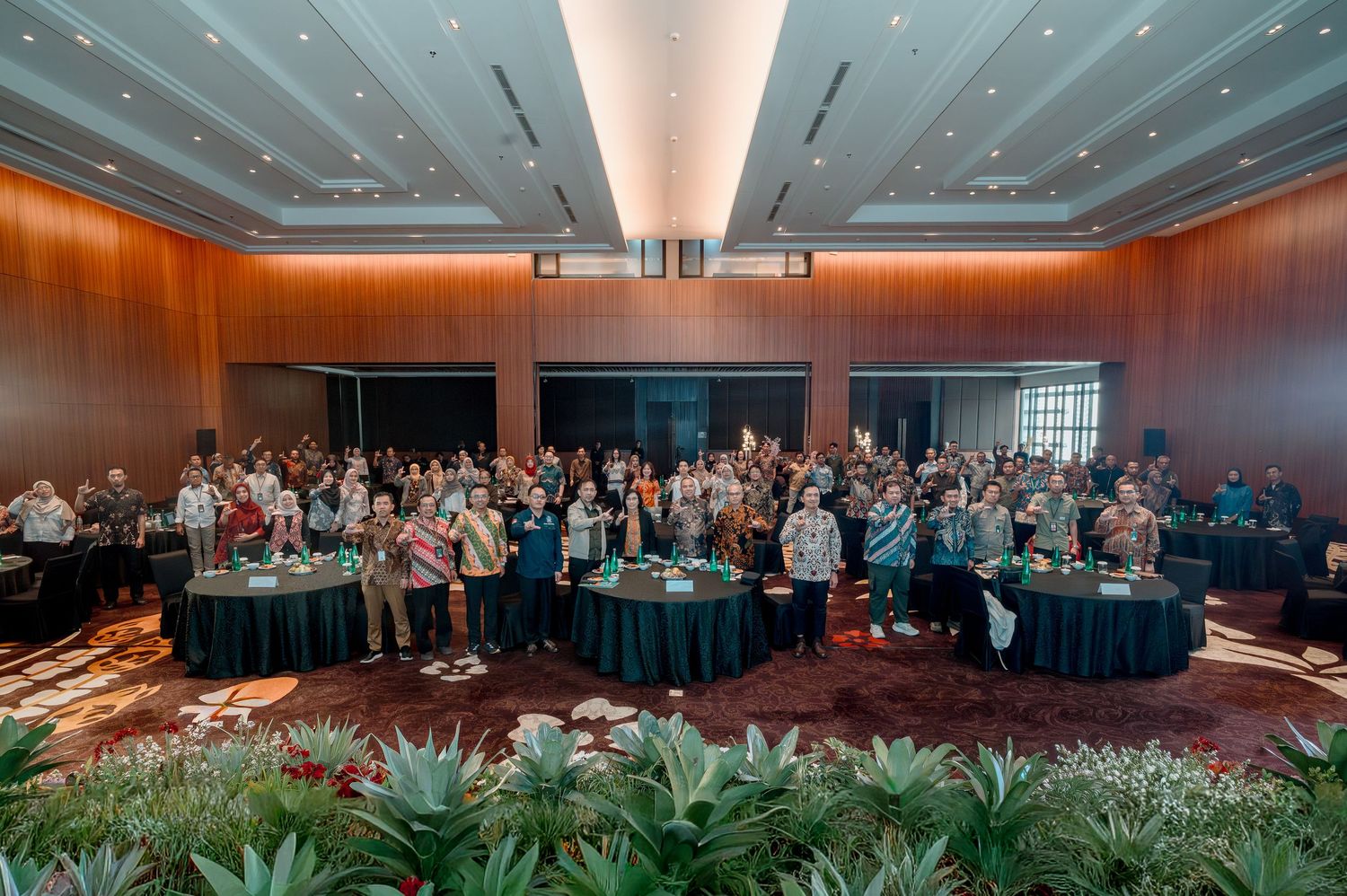 Large group of professionals posing for a group photo in an elegant hotel ballroom during a corporate conference event.