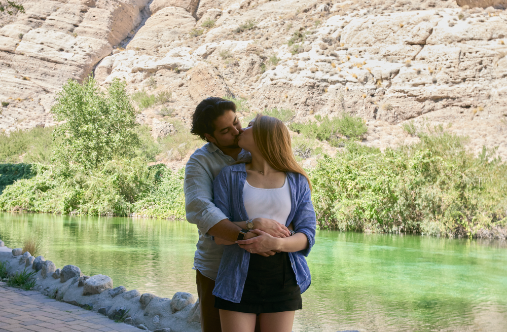 Couple sharing a romantic kiss by a serene green river with rocky canyon walls in the background.