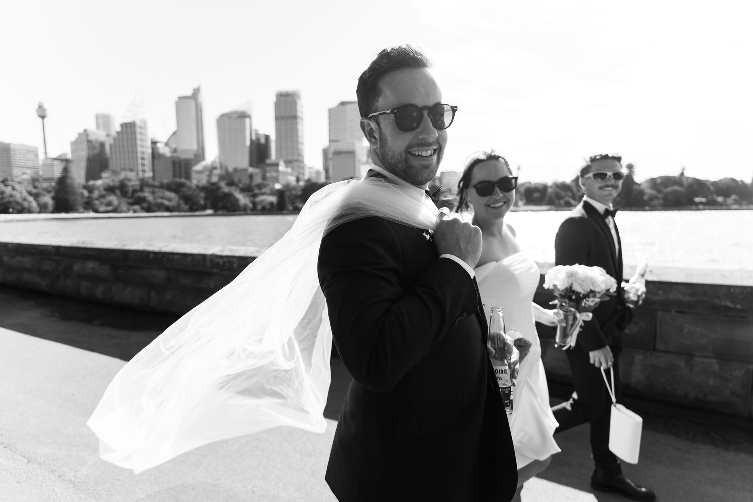 Black and white wedding photo of couple in sunglasses with Sydney city skyline backdrop.