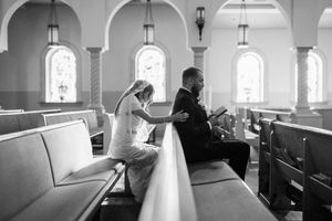 Black and white photo of a bride and groom praying in church pews before their wedding ceremony.