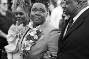 Black and white photo of an emotional person in a suit with floral corsage at a wedding ceremony.