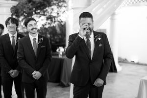 Emotional groom crying at the altar during wedding ceremony with groomsmen smiling in background.