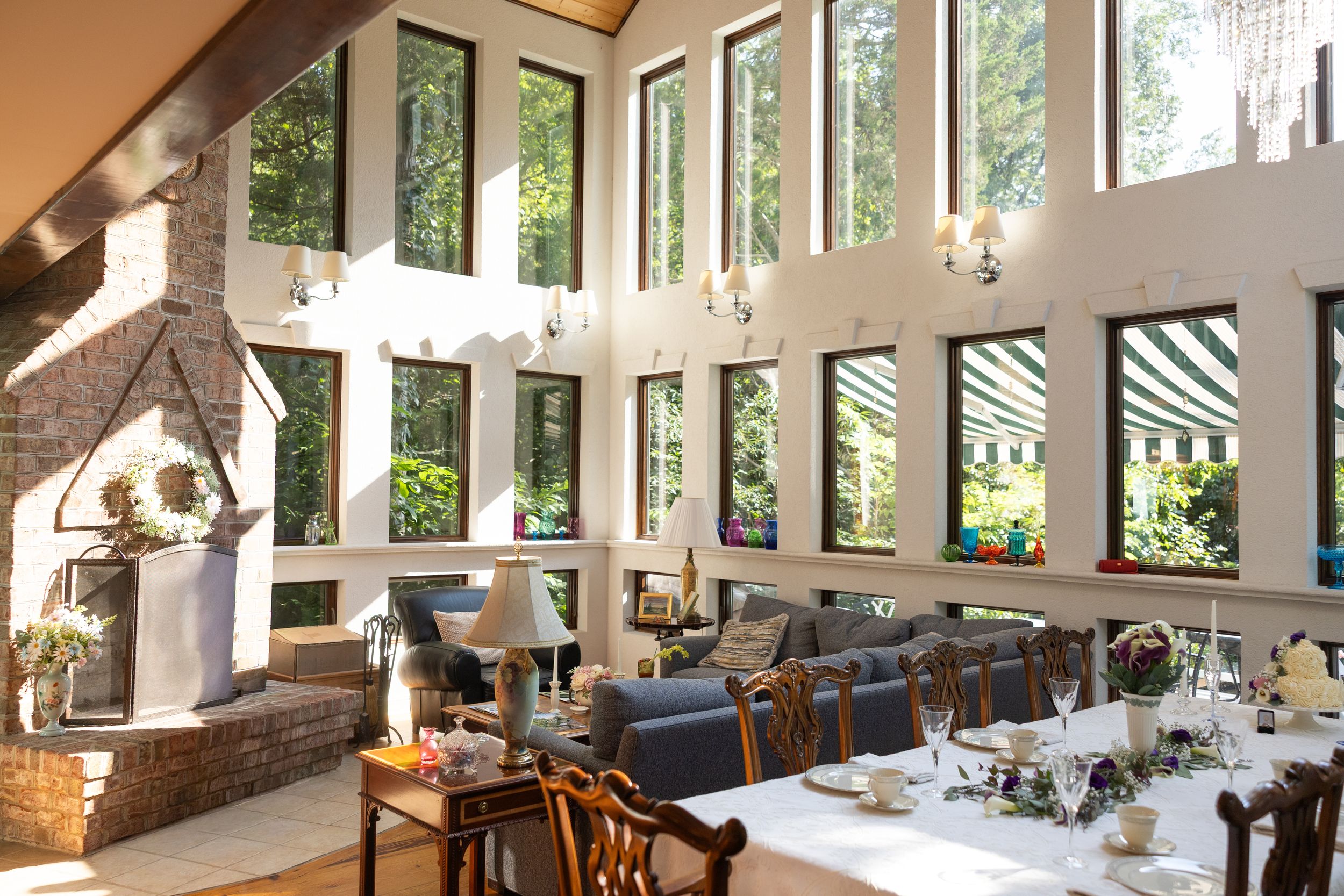 Luray, Virginia bed and breakfast dining room with floor-to-ceiling windows, set tables, and a brick fireplace surrounded by lush greenery.
