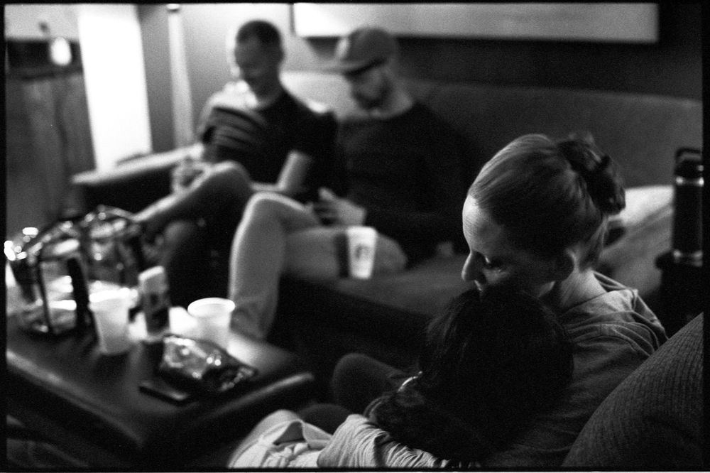 Black and white photo of a woman cuddling a child on a couch while two men sit nearby in a dimly lit room.