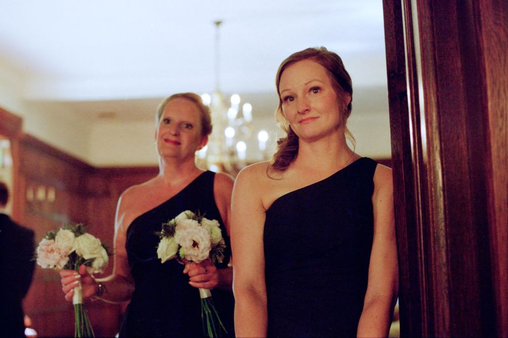 Two bridesmaids in black one-shoulder dresses hold white bouquets at an elegant wedding venue.