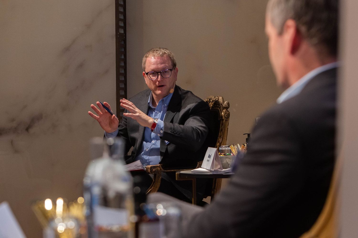 Business professional gestures during an intimate panel discussion in an elegant marble-walled venue at Grand Hotels Festvåning.