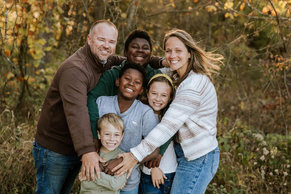 A joyful multiracial family of six hugging outdoors among autumn foliage, smiling warmly together.