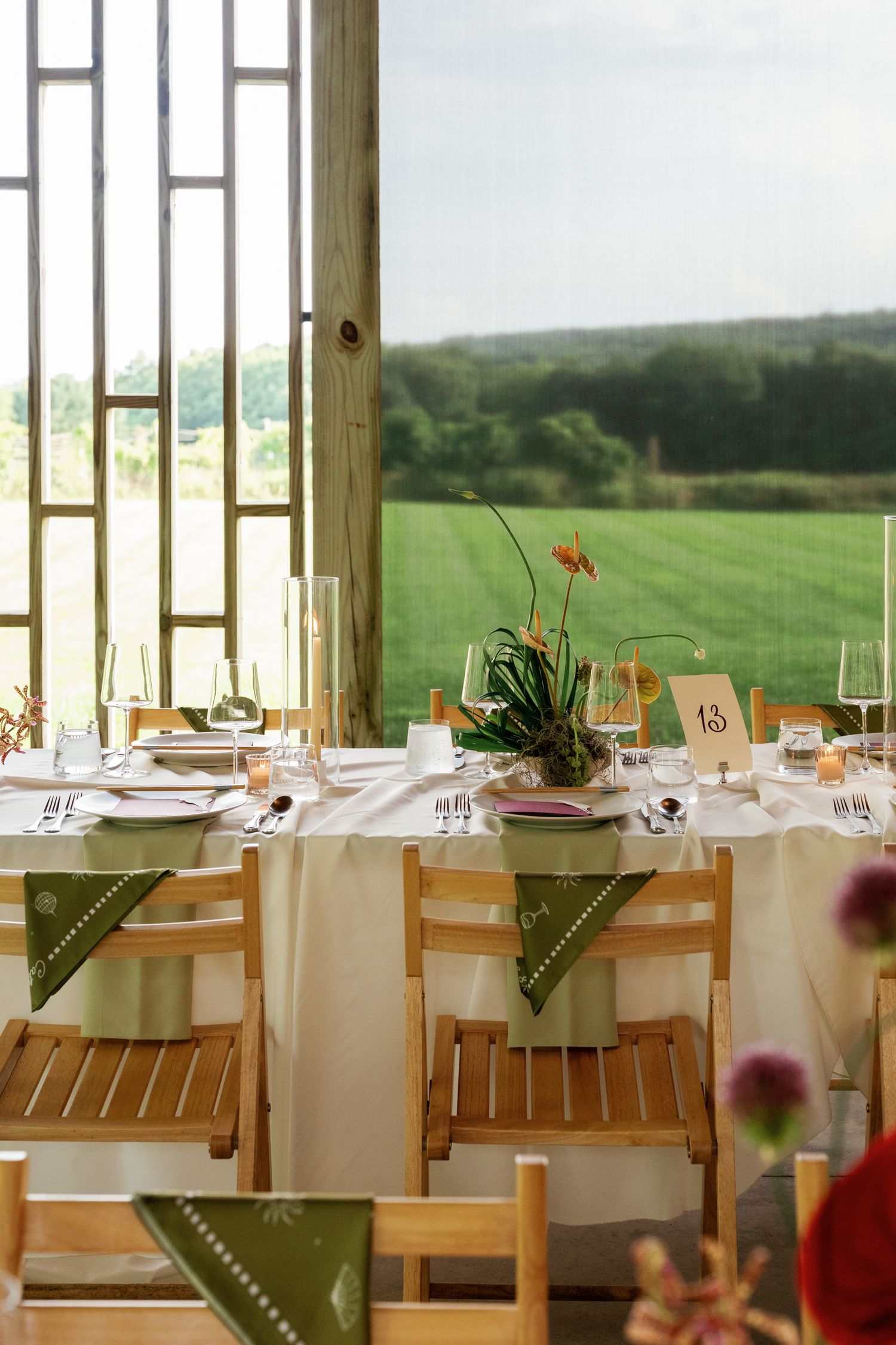 Elegant wedding reception table set with white linens, green napkins, and floral centerpiece overlooking meadow.