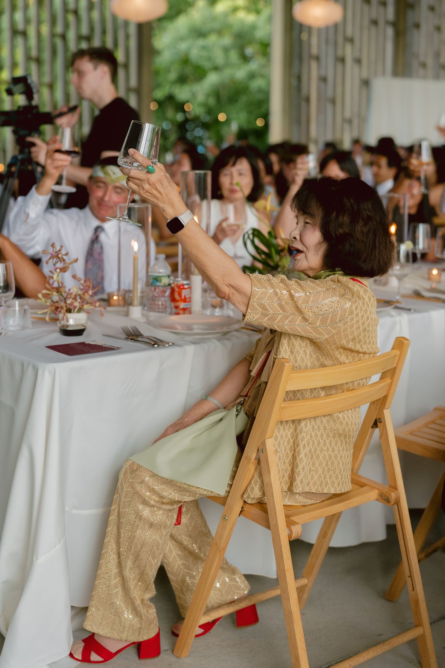 Wedding guest in gold sequin outfit raising a champagne glass during a toast at a reception dinner.