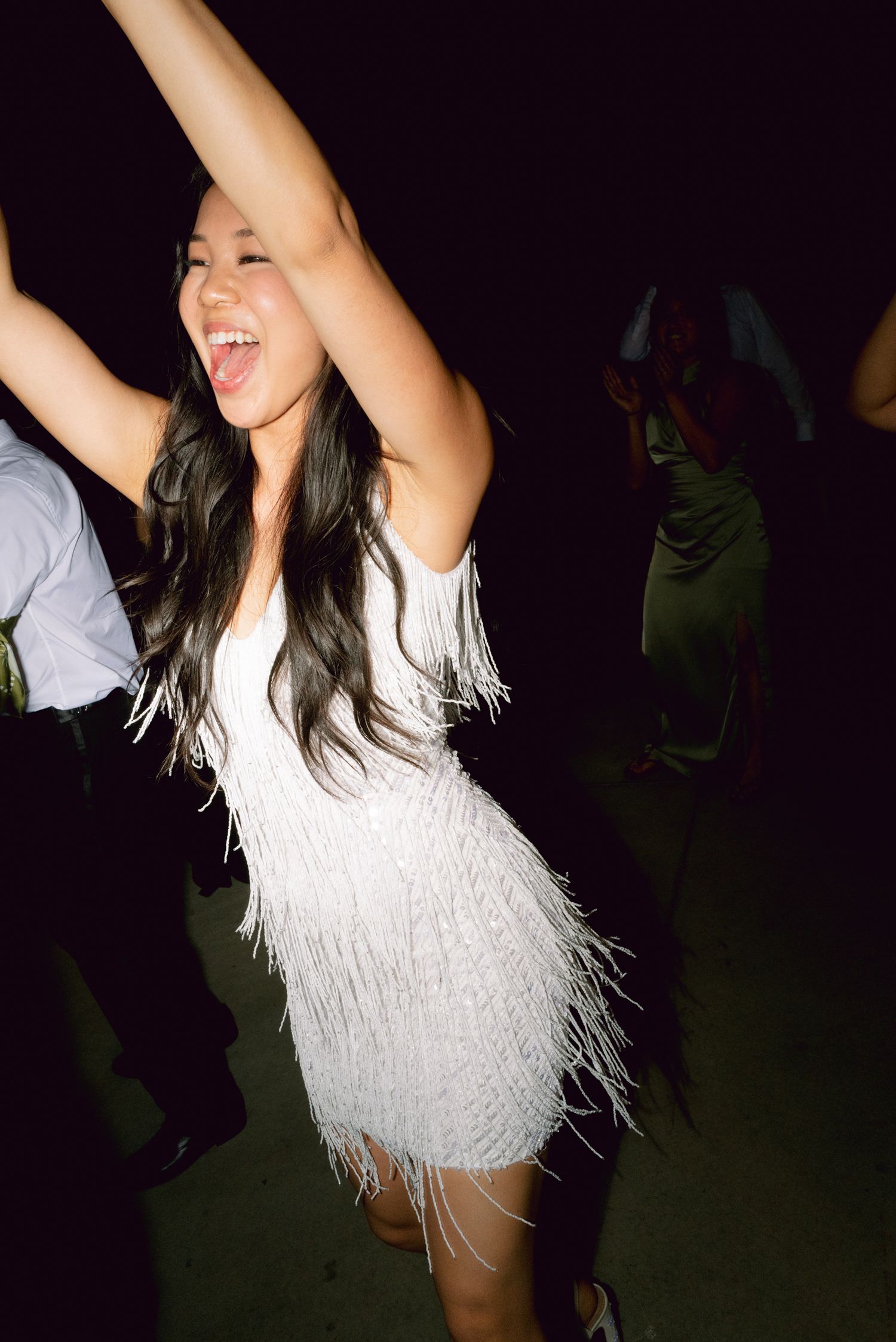 Bride in white fringe mini dress dancing joyfully at lively wedding reception party.