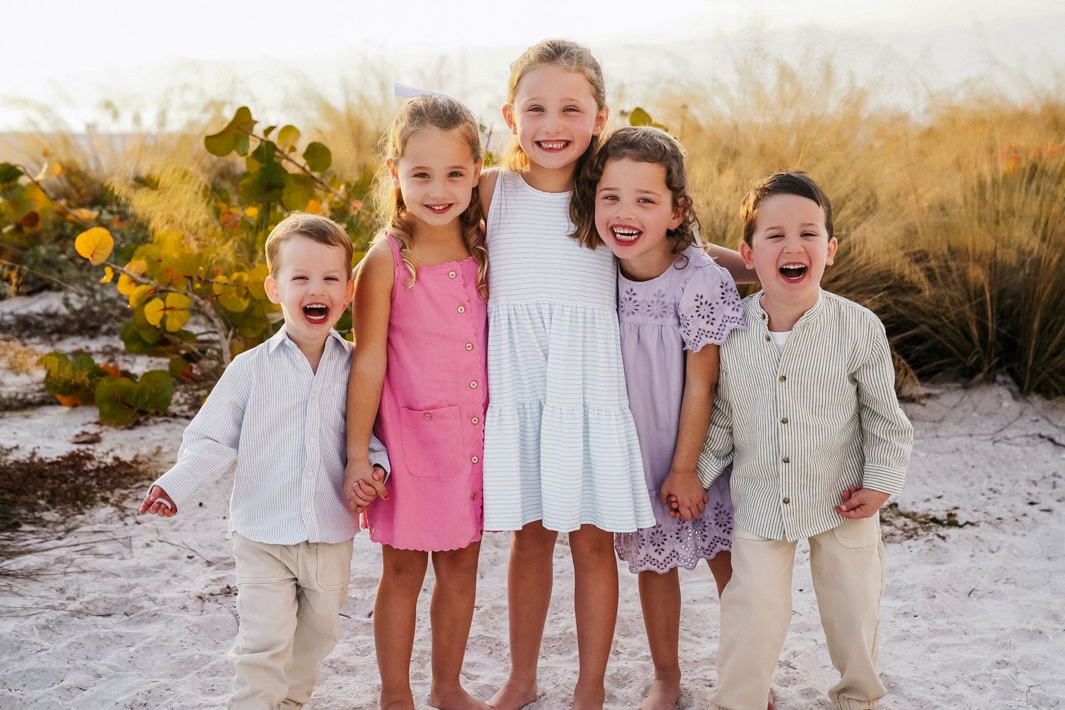 Family of five smiling together on a beach at sunset, wearing coordinating blue outfits.