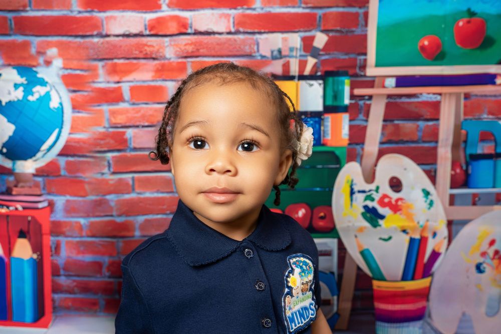 Adorable toddler in navy school uniform poses in front of colorful classroom-themed backdrop.