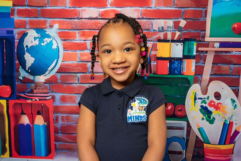 Happy young girl with braids in navy school polo smiles before colorful educational backdrop.